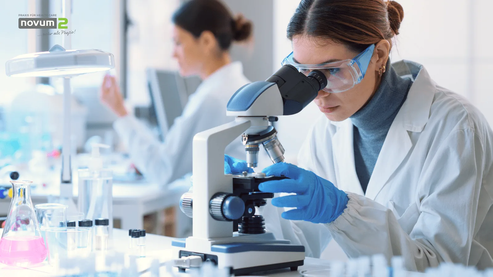 Researcher with safety goggles examines samples under a microscope in a Novum2 laboratory for advanced health research