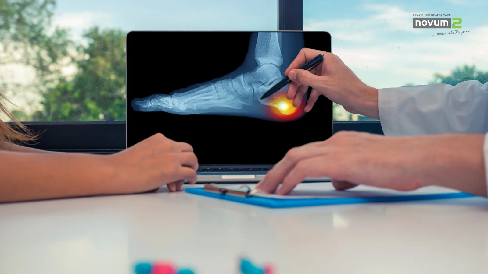 Doctor explains the diagnosis of heel pain to a patient using an X-ray image on a laptop at the Novum2 physiotherapy practice