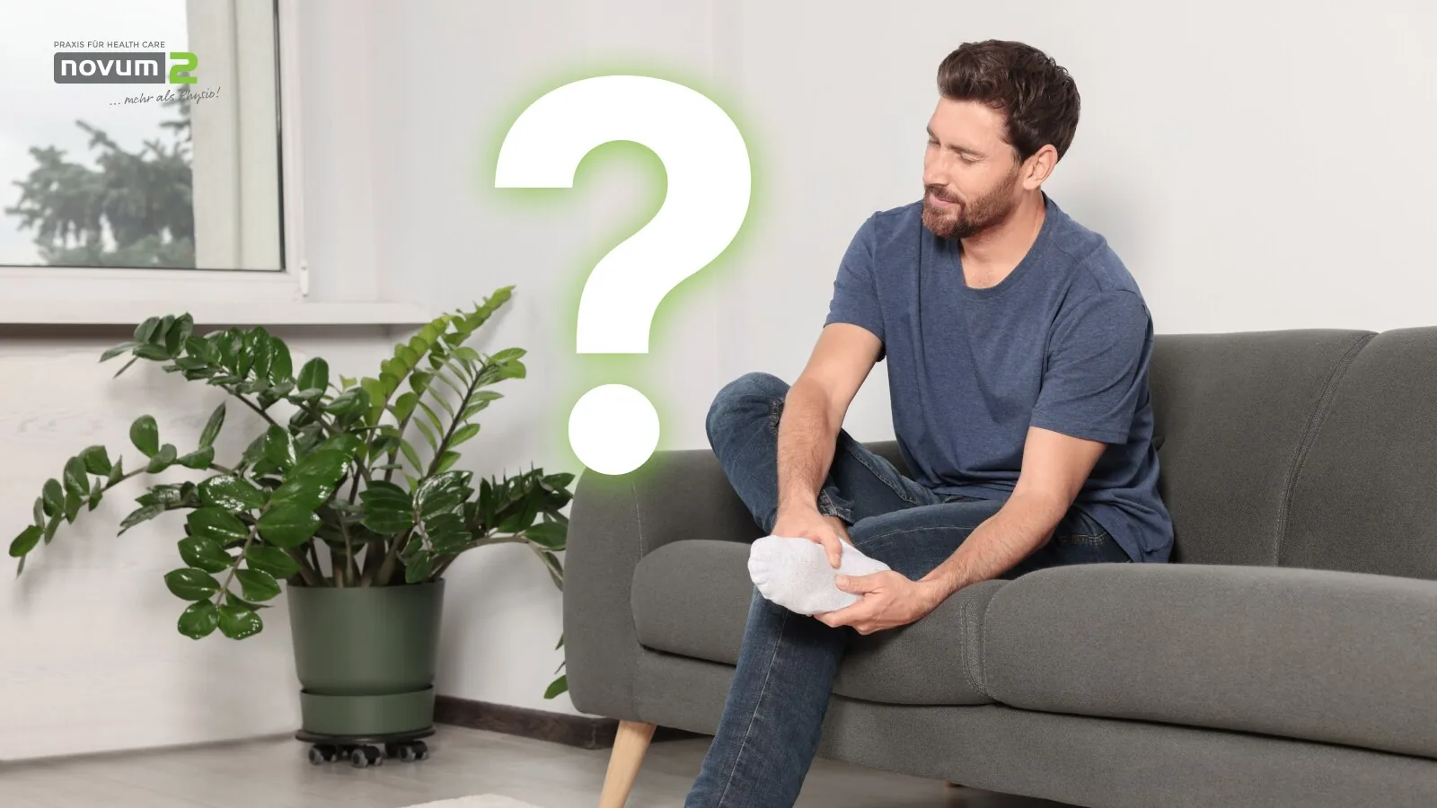 Man sitting on the sofa holding his aching foot, with a question mark in the background, at the Novum2 physiotherapy practice